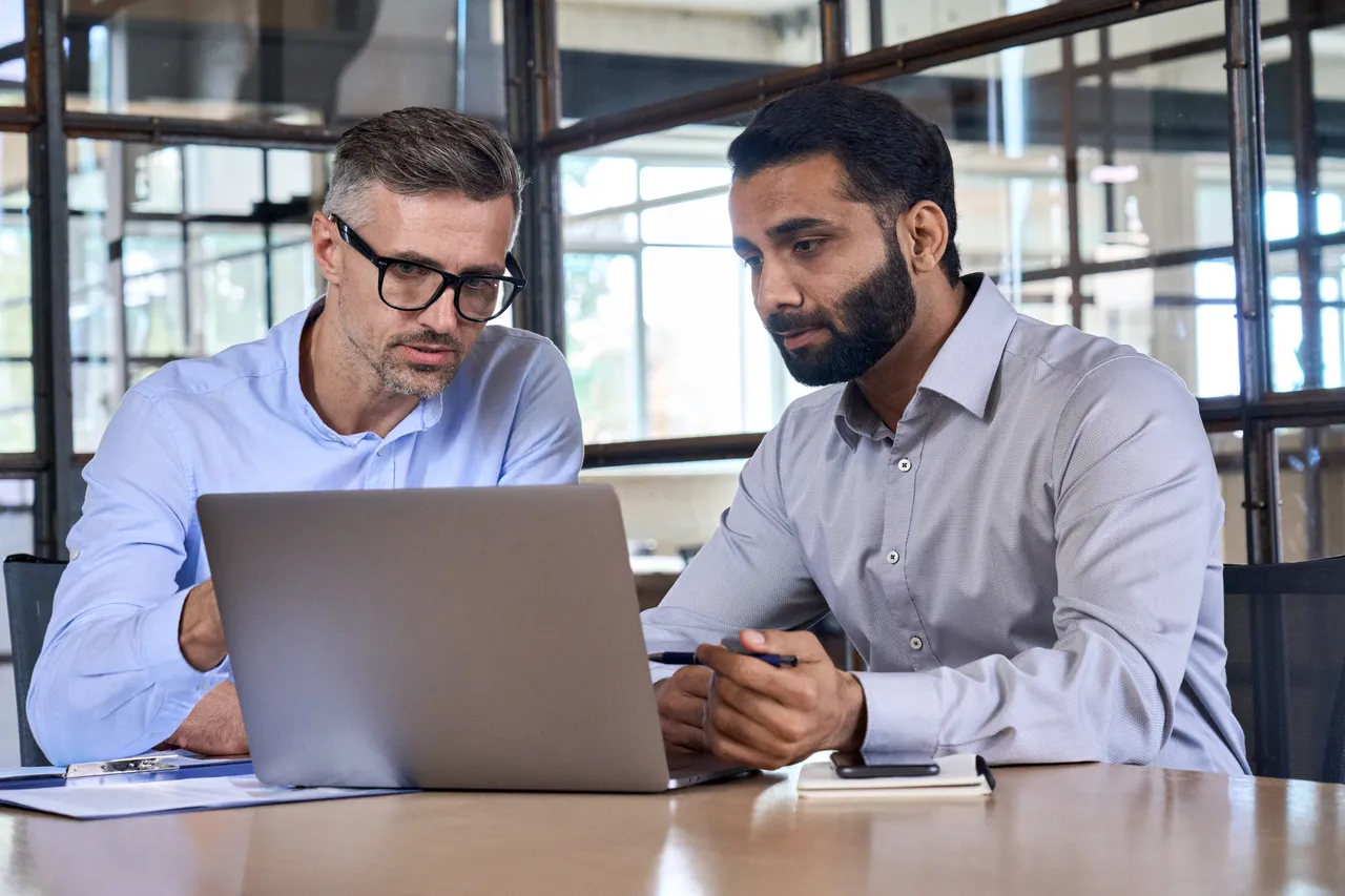 An AI-generated image of two colleagues talking over a laptop.